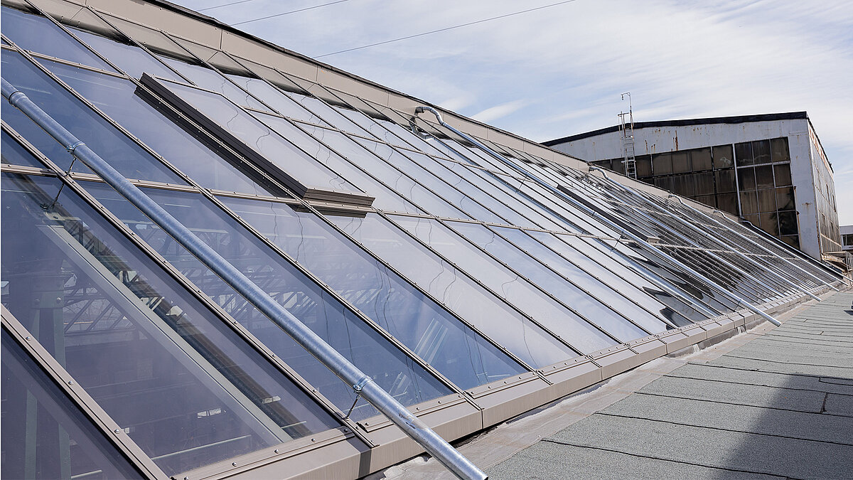 Modern glass roof of the Factory Campus in Düsseldorf with reflective sky.