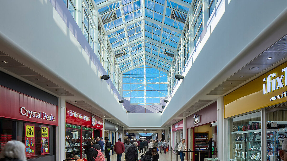 Shopping mall with glass roof and shops, natural light streaming in