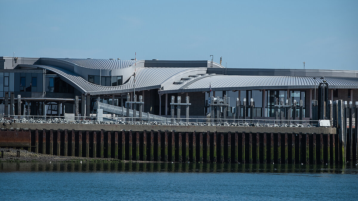 Norderney ferry terminal with modern, wave-shaped roof and glass facades by the water.