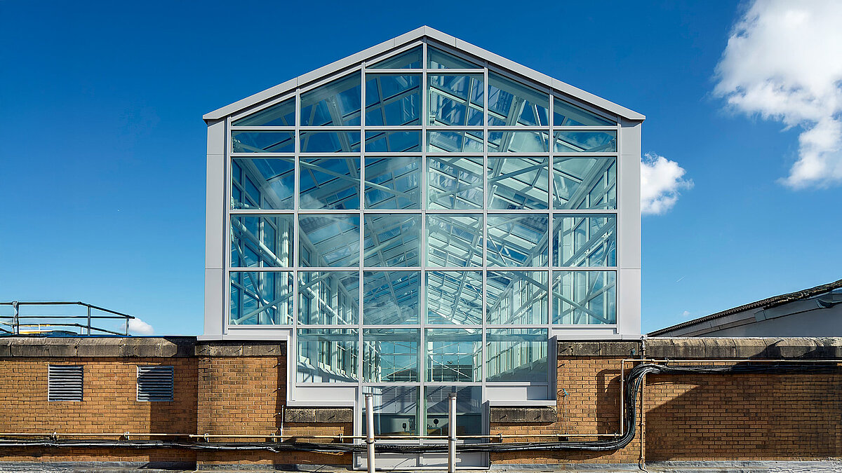 Modern glass roof with steel frame on an industrial building, blue sky and clouds reflected in the glass