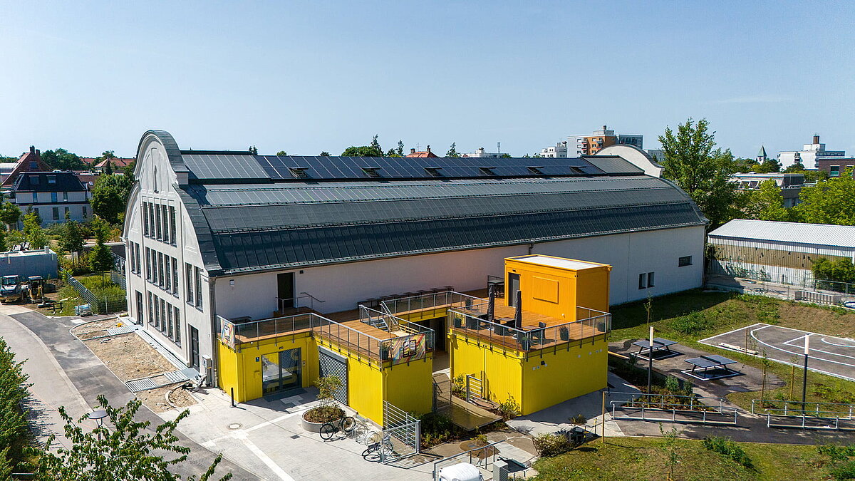 Renovated industrial building with LAMILUX glass roof and photovoltaics, yellow annexes in the foreground.