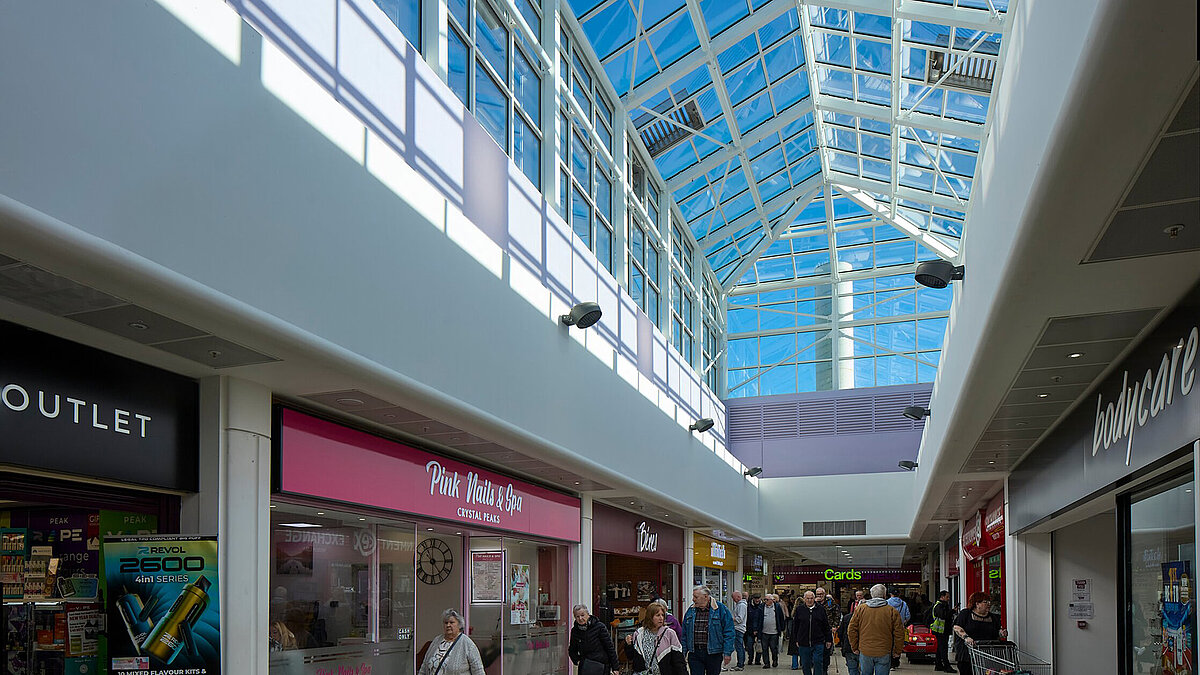 LAMILUX glass roof with blue metal structure over a shopping mall with shops and people, daylight