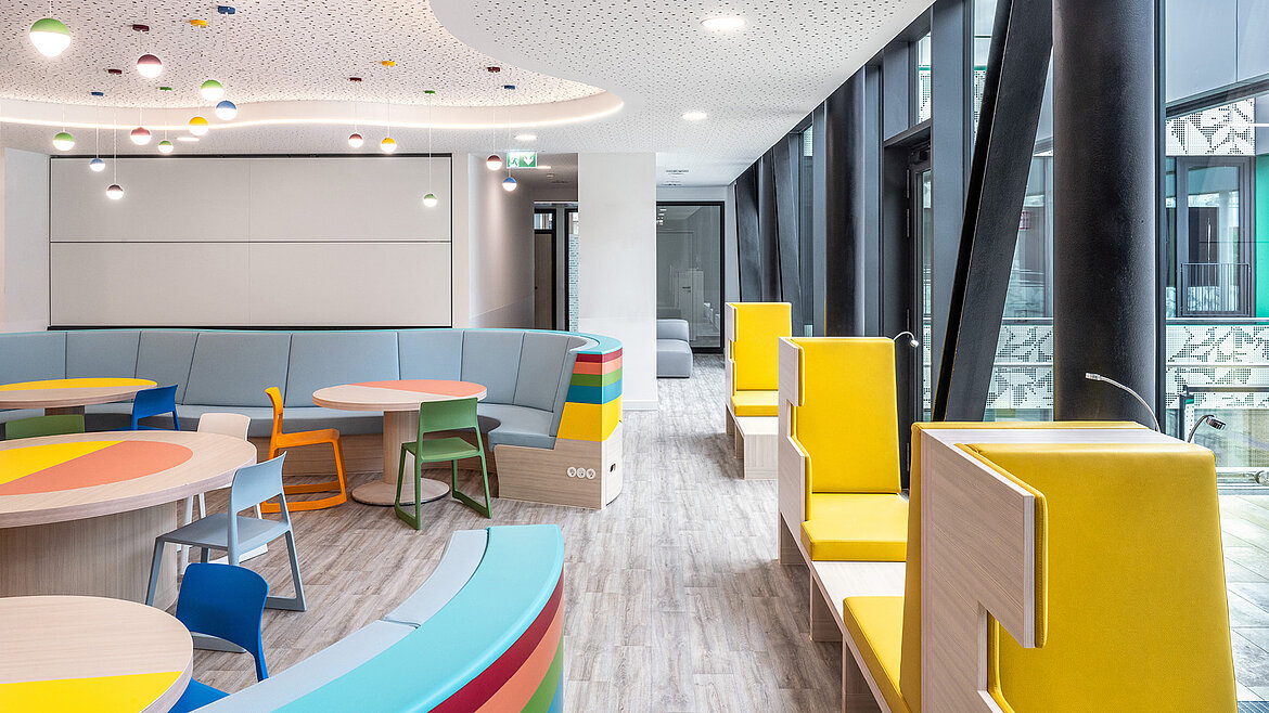 Modern, colourful lounge with bright furniture and large windows.