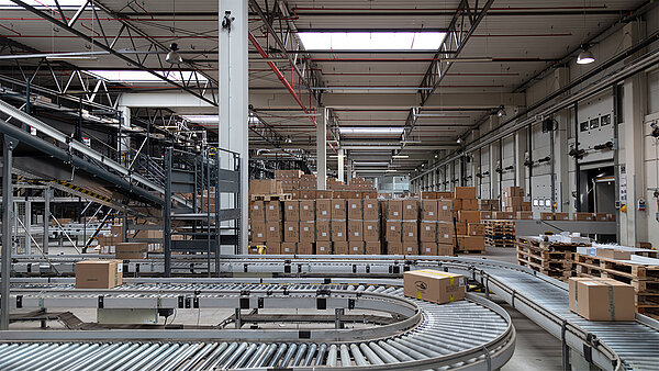 Förderband mit Paketen in einer Industriehalle mit LAMILUX Lichtbändern auf dem Dach