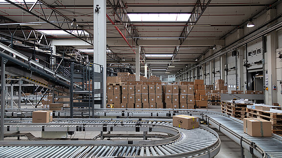 Förderband mit Paketen in einer Industriehalle mit LAMILUX Lichtbändern auf dem Dach