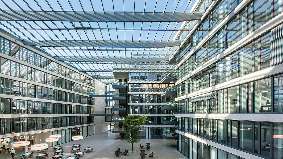 Modern atrium of the FGS Campus with a large glass roof, sunlit spaces, multiple floors, and seating areas in the open space.