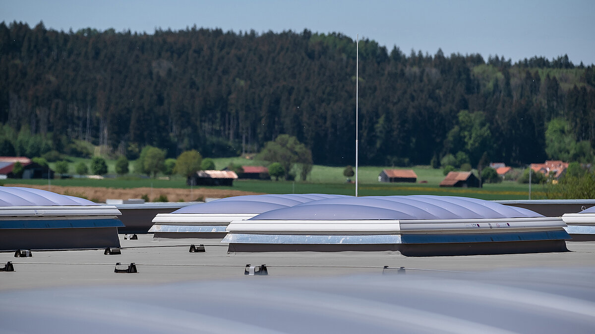 LAMILUX F100 W skylights on the roof of the Unglehrt construction company's production hall, surrounded by rural landscape with trees and farmhouses.