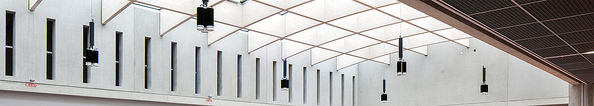Modern atrium in Willibald-Gluck-Gymnasium in Neumarkt with LAMILUX glass roof, concrete walls, and colorful floors.