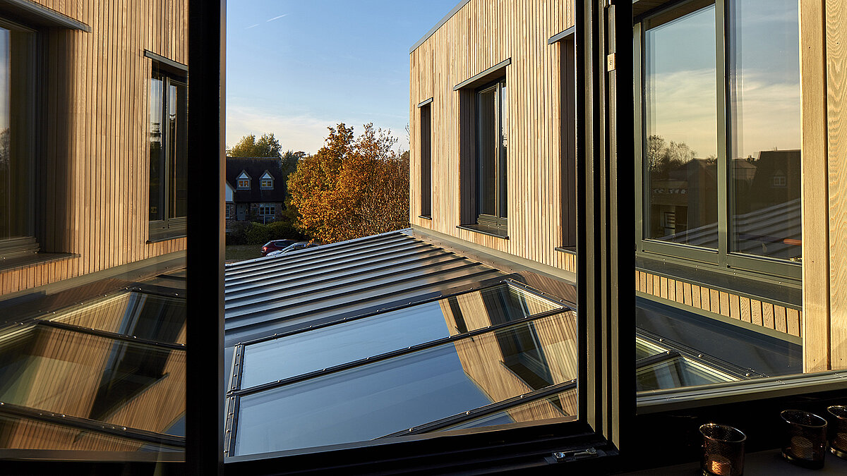 View through a window of the glass roof and facade of the Potton Show Homes in England bathed in warm sunlight.