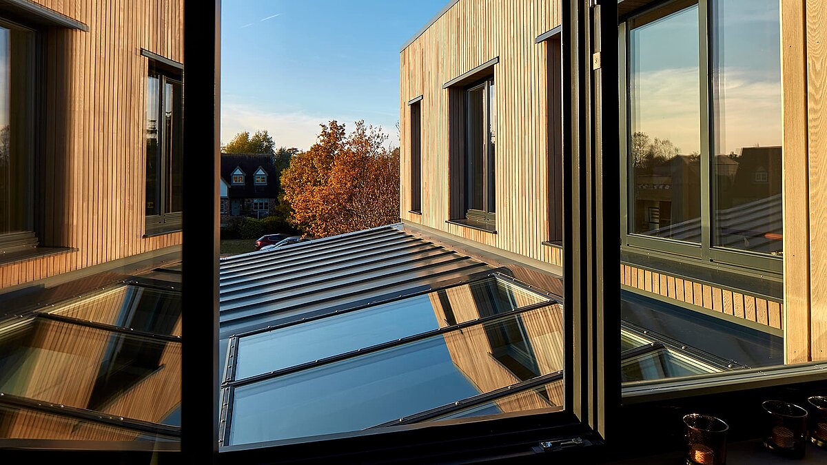 View through a window of the glass roof and facade of the Potton Show Homes in England bathed in warm sunlight.