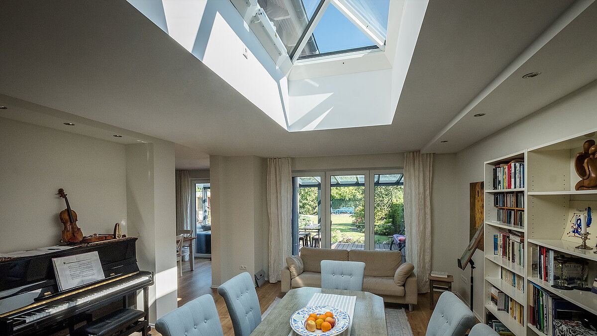 Living room in a residential house in Hamburg with a LAMILUX FW flat roof window, bringing natural light onto the dining table and bookshelves.