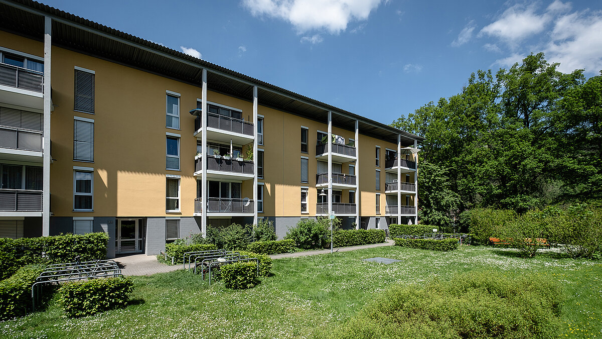 Apartment building in Freiburg with a yellow facade, balconies, and a green outdoor area.