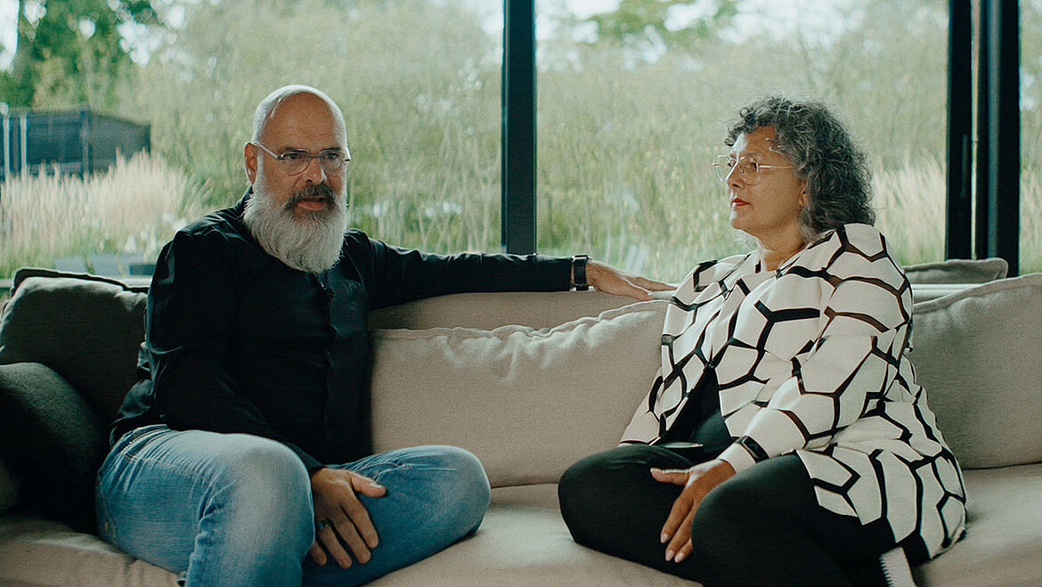 Two people sitting opposite each other on a sofa in a modern interior space, engaged in a relaxed conversation