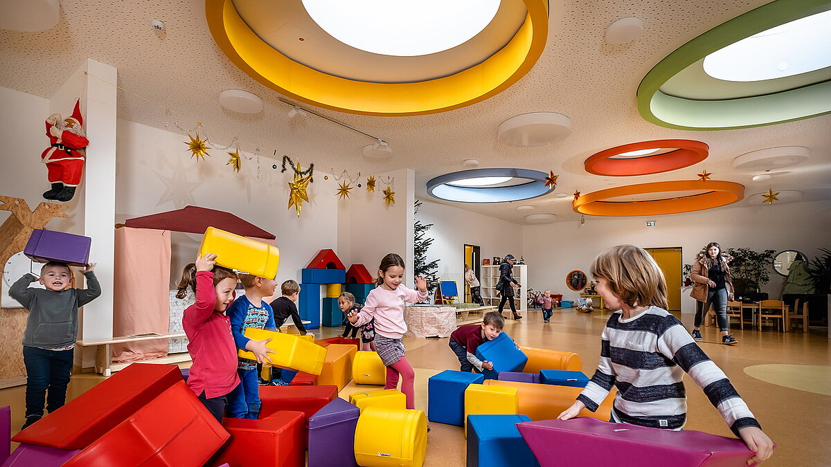 Children play with colourful building blocks under colourful, round ceiling windows at the Glückliche Zukunft daycare centre in Sömmerda.