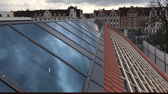 Modern glass roof with a red tiled roof in the construction phase at Leibniz University Hanover, with historical buildings in the background.