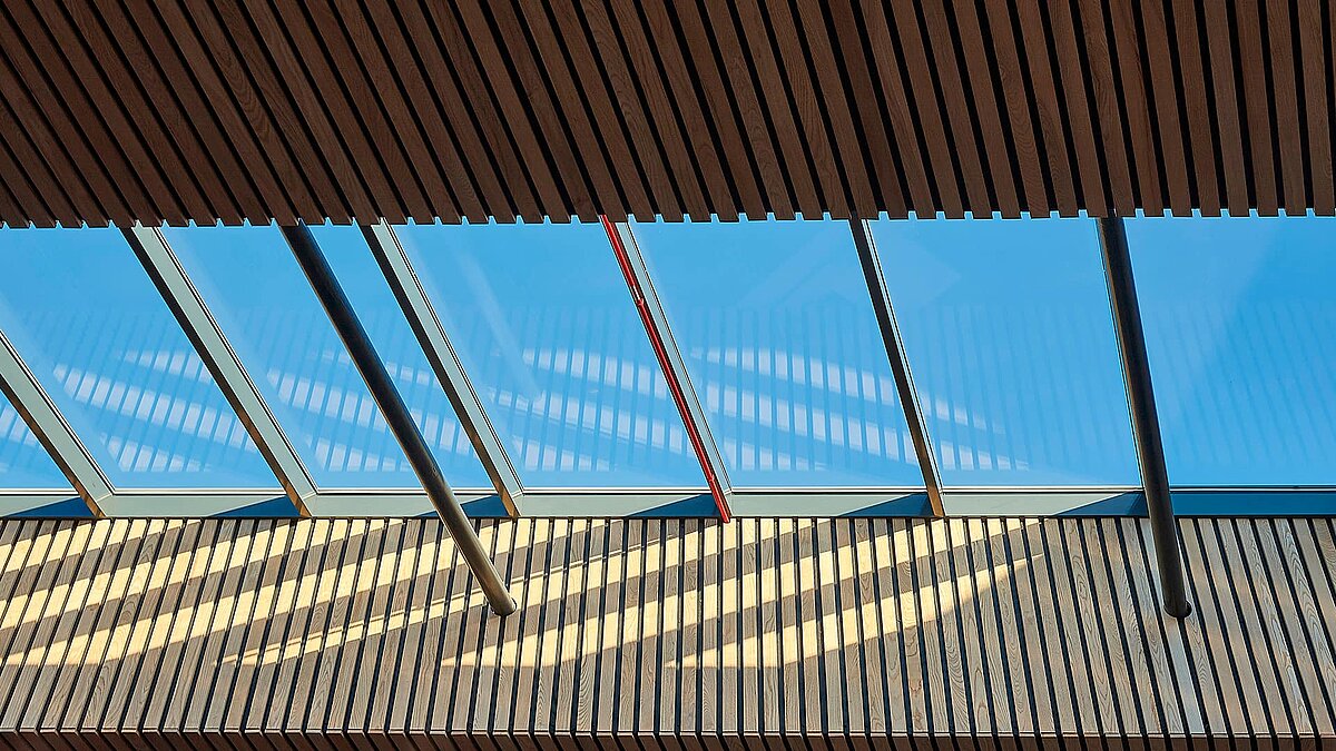 Interior view of the LAMILUX PR60 glass roof at Sheffield Hallam University with wooden elements and shadow patterns.