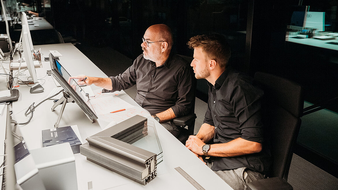 Two men in black clothing working together at a computer workstation.