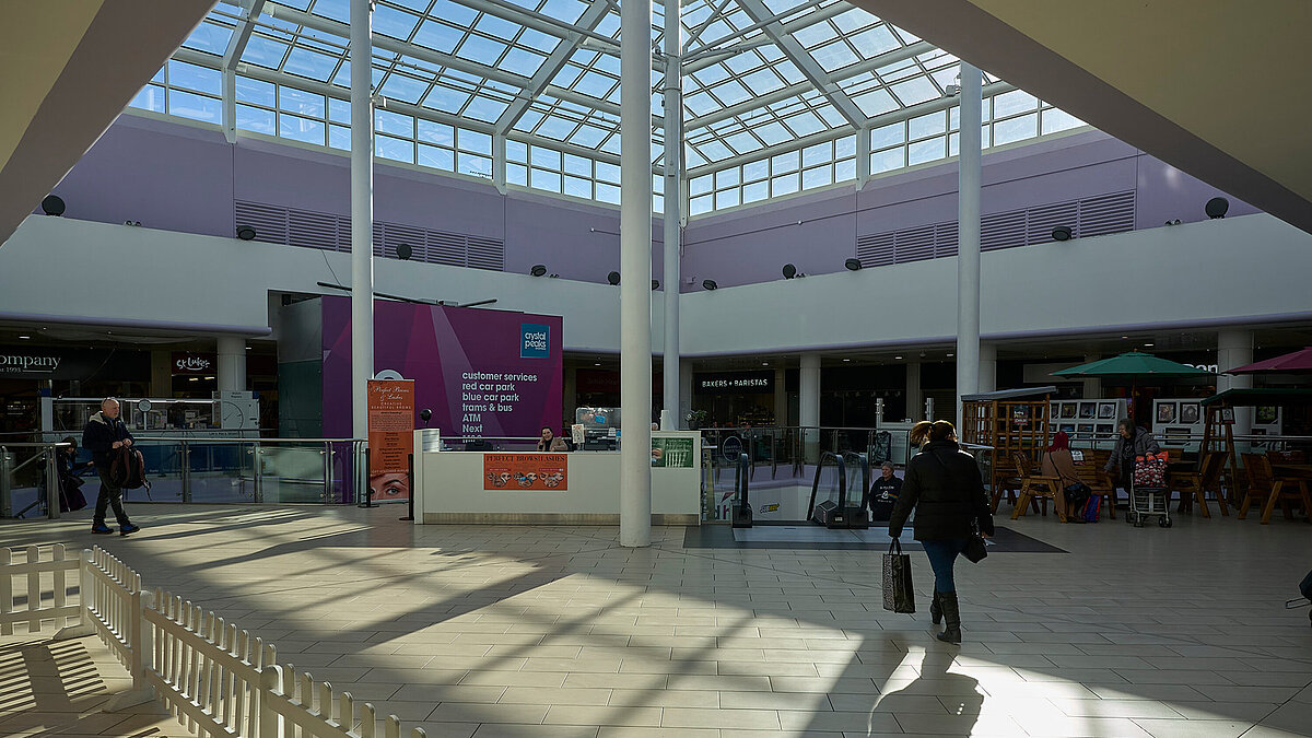 Interior of a shopping mall with glass roof and sunlight, people walking and shopping