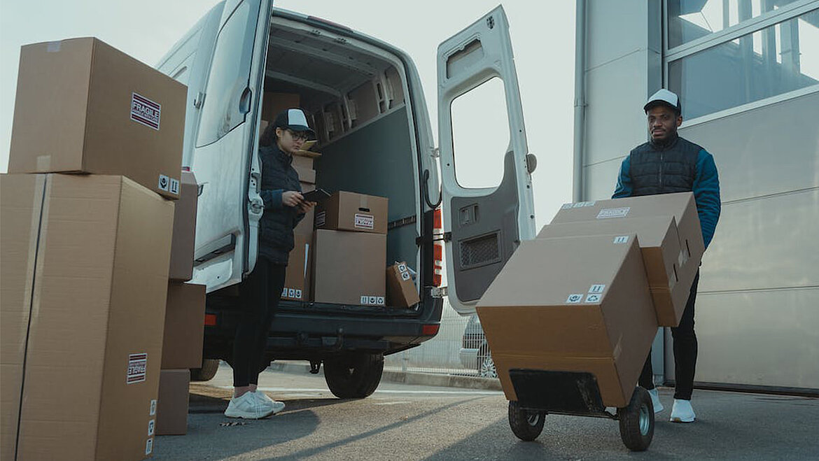 Employees unload delivery trucks filled with boxes using hand trucks
