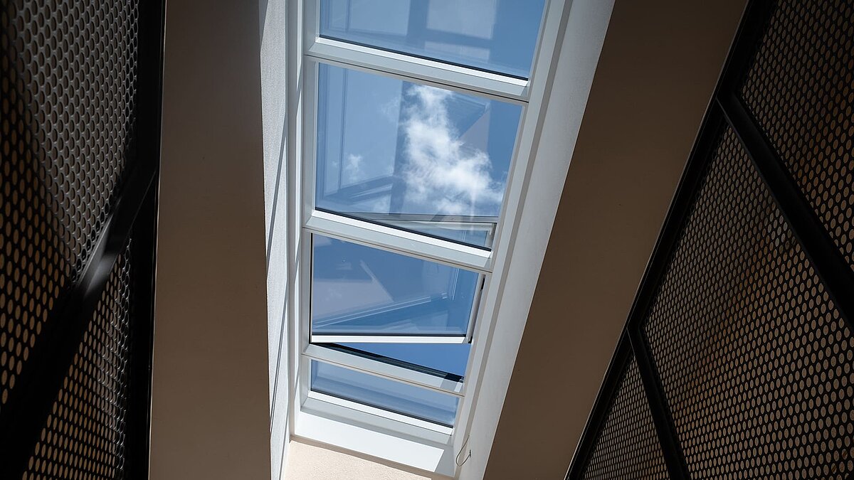View through a modular glass roof by LAMILUX in a residential building in Freiburg, reflecting the sky and clouds.