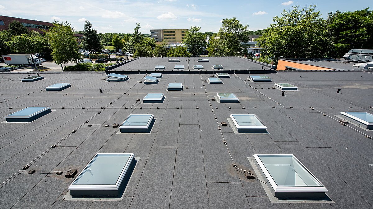 Flat roof at Caritas Hagen with multiple rectangular skylights and surrounding green landscape.
