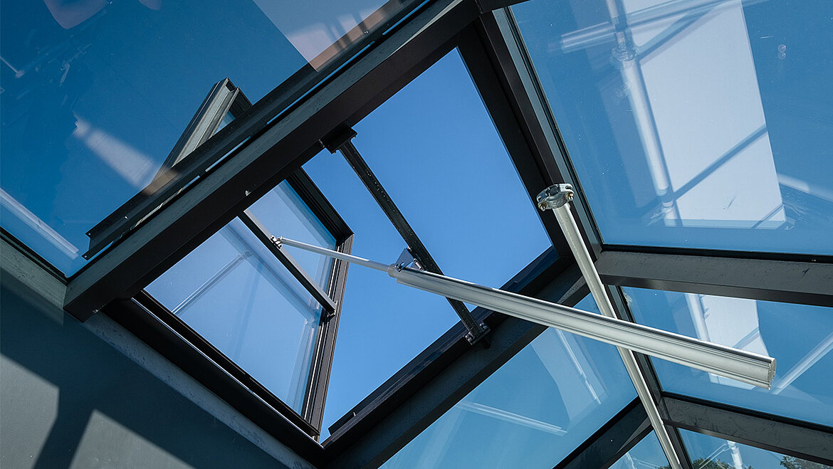 An open skylight with an aluminium frame and silver struts against a blue sky