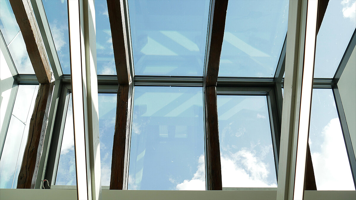 Modern glass roof of Leibniz University Hannover with visible wooden beams and sky reflections.
