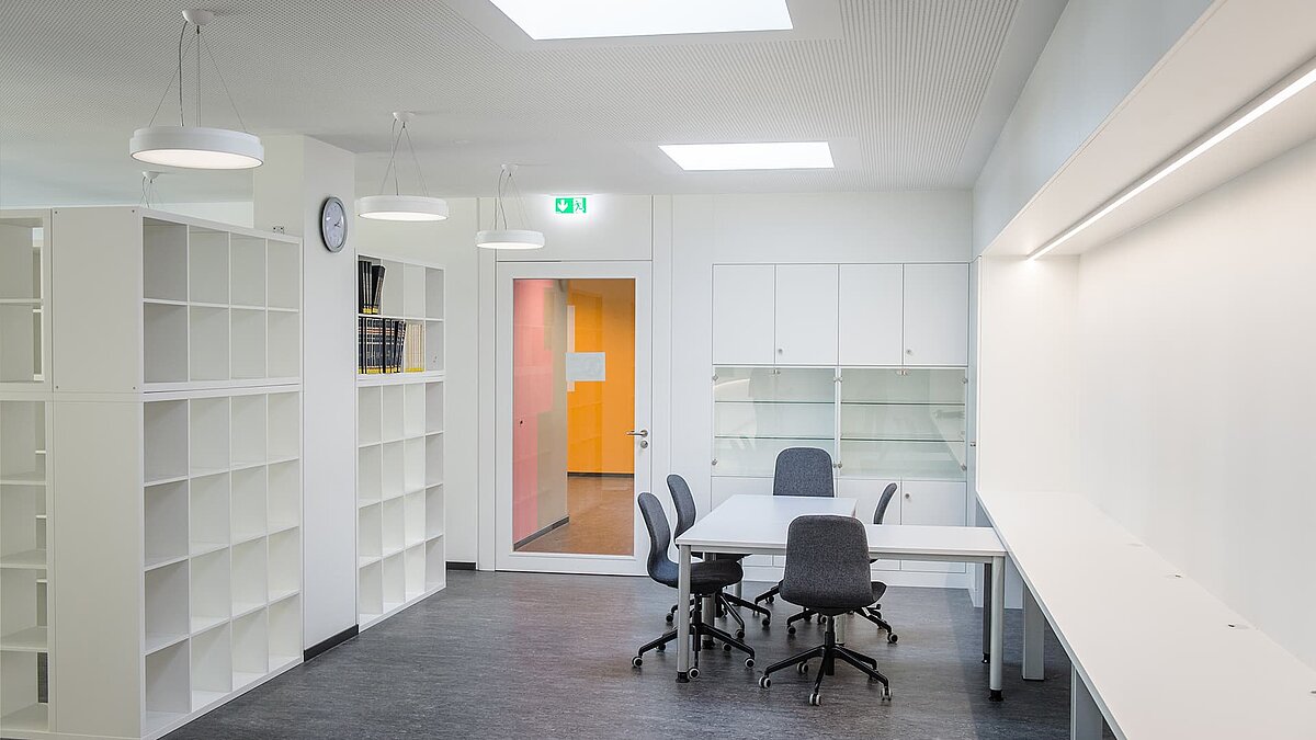 Bright workspace at Markgraf-Georg-Friedrich-Gymnasium in Kulmbach featuring flat roof windows, modern shelves, tables, and chairs.