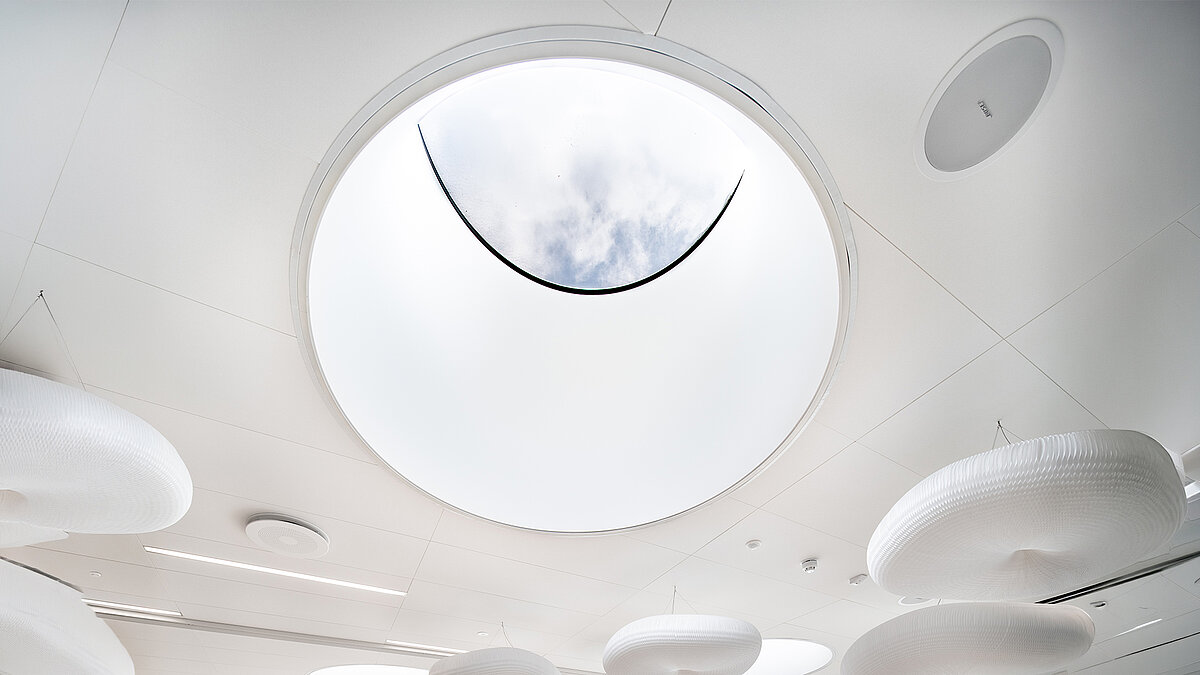 Circular skylight in the ceiling of the Ernst & Young office building with view of the sky and modern suspended lighting elements