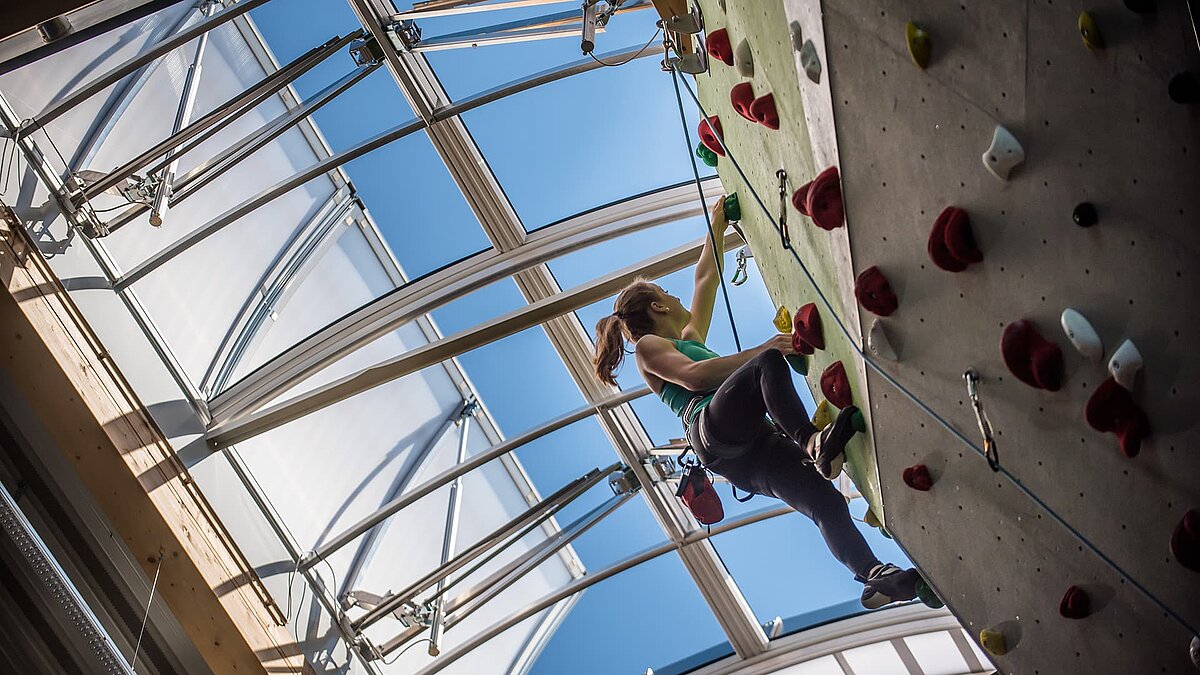 Female climber on an indoor climbing wall at the OWL climbing center under a large skylight providing natural daylight.