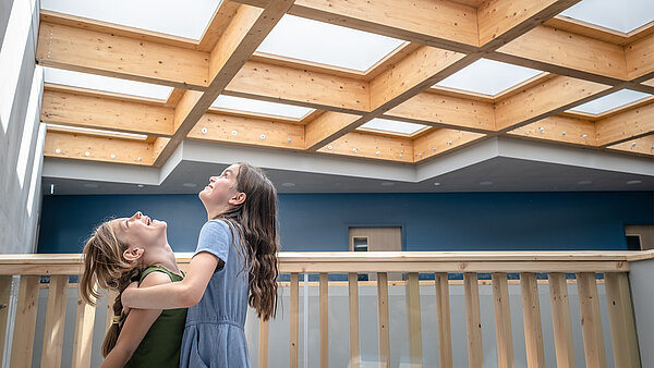 Two girls are standing on a wooden balcony, looking up at the ceiling 