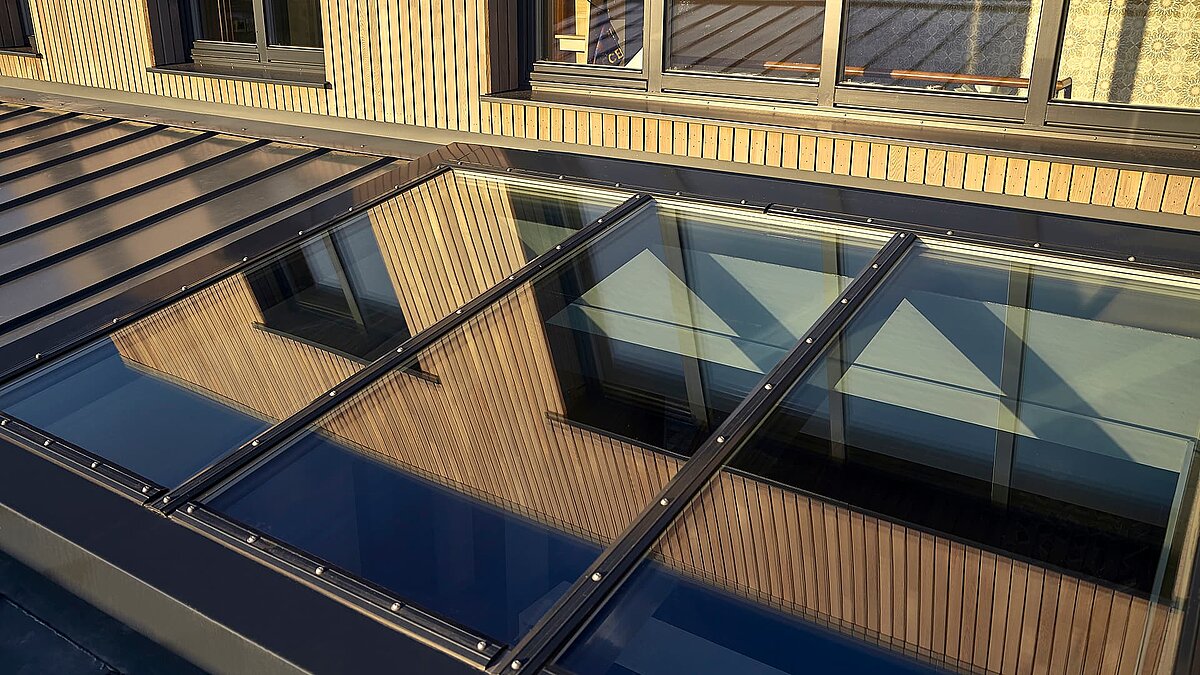 Close-up view of the LAMILUX PR60 glass roof at Potton Show Homes in England, reflecting the wooden facade and windows.