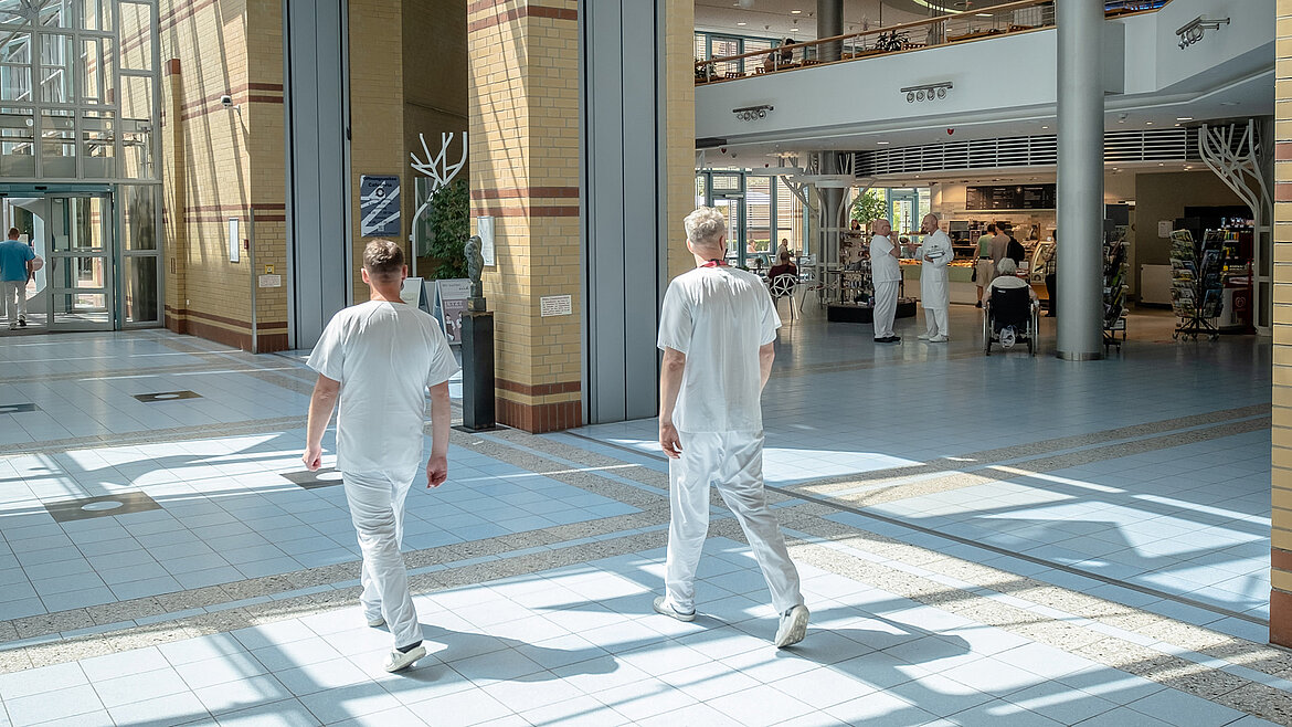 Two hospital employees walk through a light-filled hospital atrium with a glass roof.