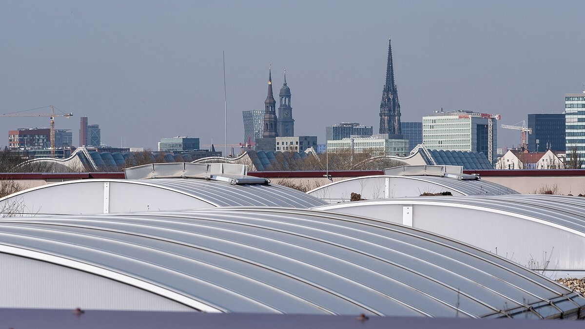 Flat roof with curved skylights at the Hamburg State Opera's storage facility, with the Hamburg skyline in the background.