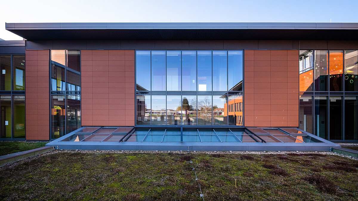 Exterior view of the Rehau school center featuring a LAMILUX PR60 glass roof above a green rooftop area.