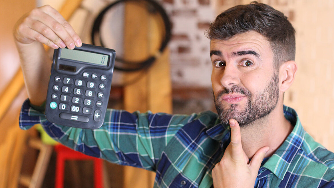 Man with beard and sceptical expression holding up a calculator