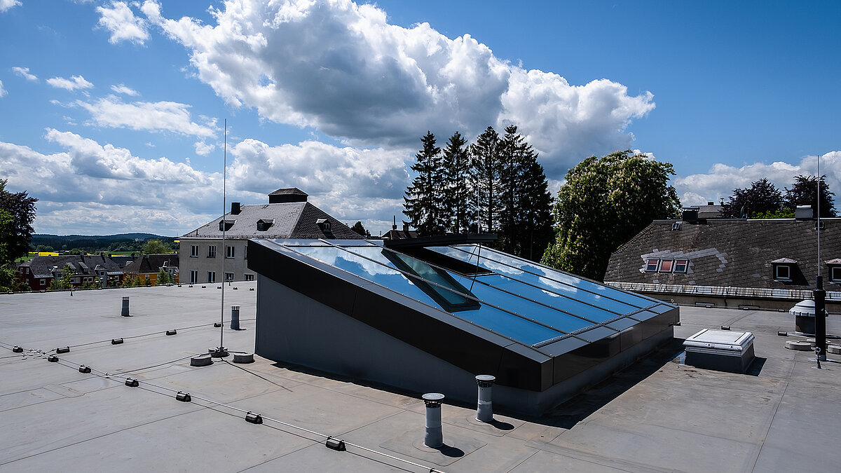 Sloped glass roof on a flat roof, modern roof glazing with an open ventilation flap under a blue sky