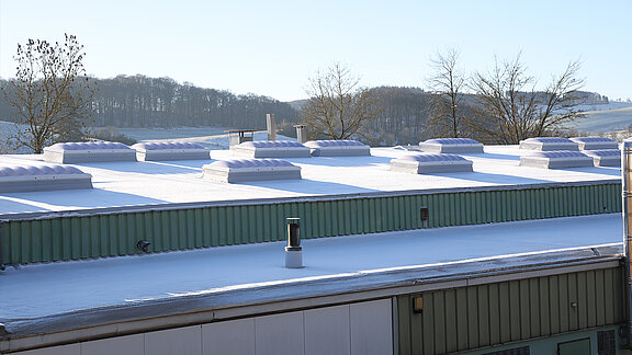 Snow-covered flat roof of the "Ab in die Box" building at Diemelsee with wave-shaped skylights.