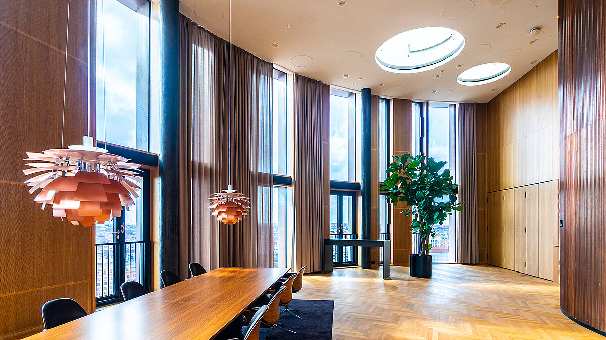 Bright conference room with large wooden table, floor to ceiling windows and two circular skylights