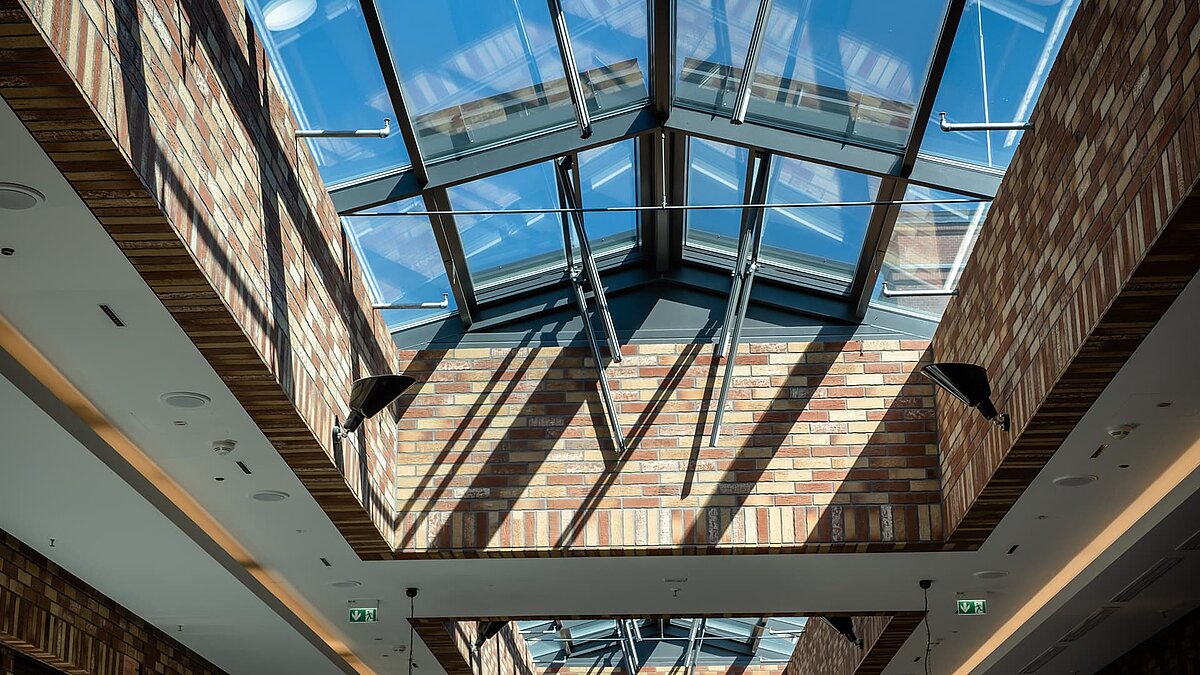 Glass roof of the Schultheiss Quartier in Berlin-Moabit, with natural light streaming in and brick walls creating shadow patterns.