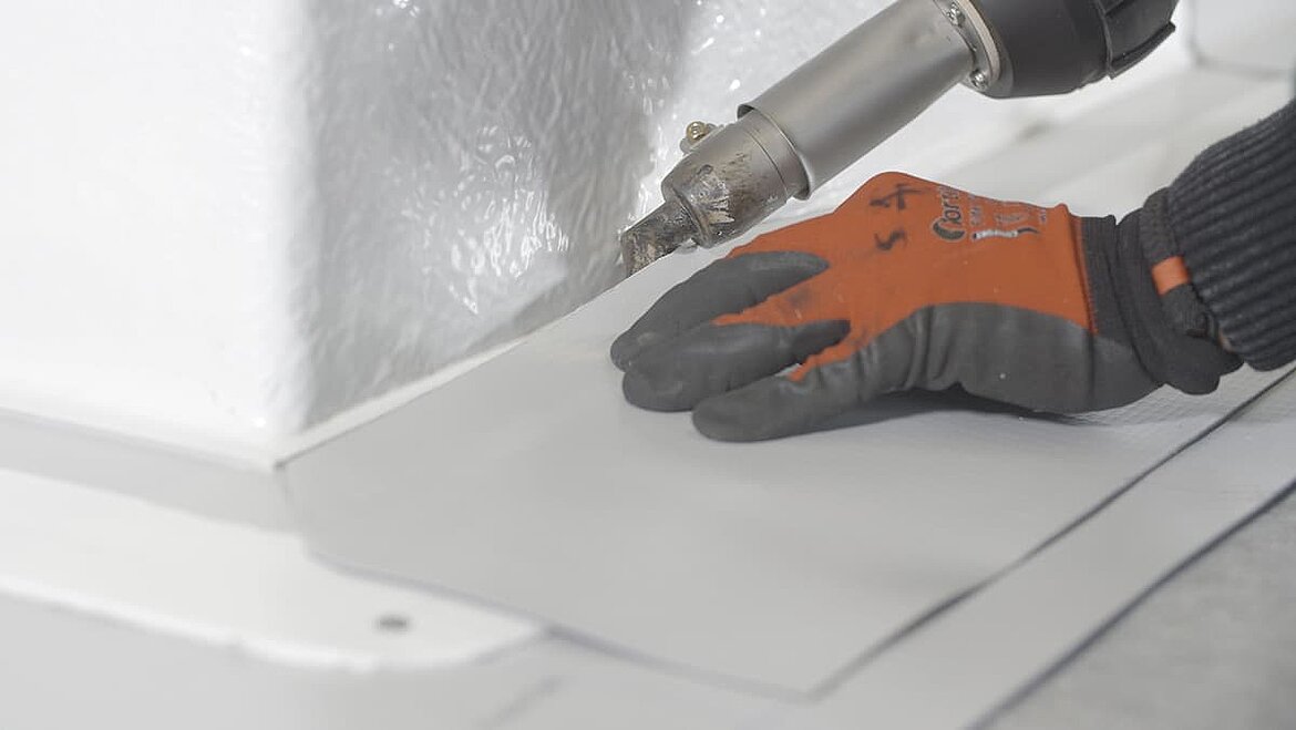 Hand with protective gloves welding roof membrane with hot air tool.