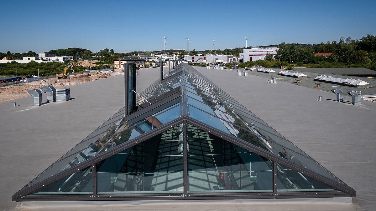 Large glass roof on the flat roof of the Outlet Center Selb, with surrounding industrial area and wind turbines in the background.