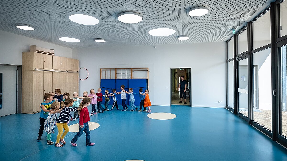 Gymnasium at the Sonnenfeld day care centre in Wandlitz with children playing, blue floor, round skylights and modern equipment.