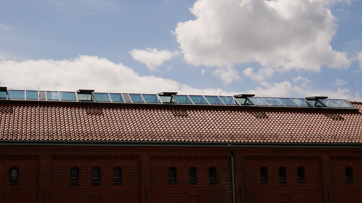 Red tiled roof with modern glass skylights at Leibniz University Hannover under a blue sky with clouds.