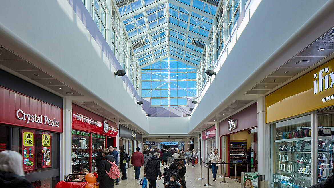 Modern shopping mall with wide corridor, glass ceiling and numerous fashion stores on both sides