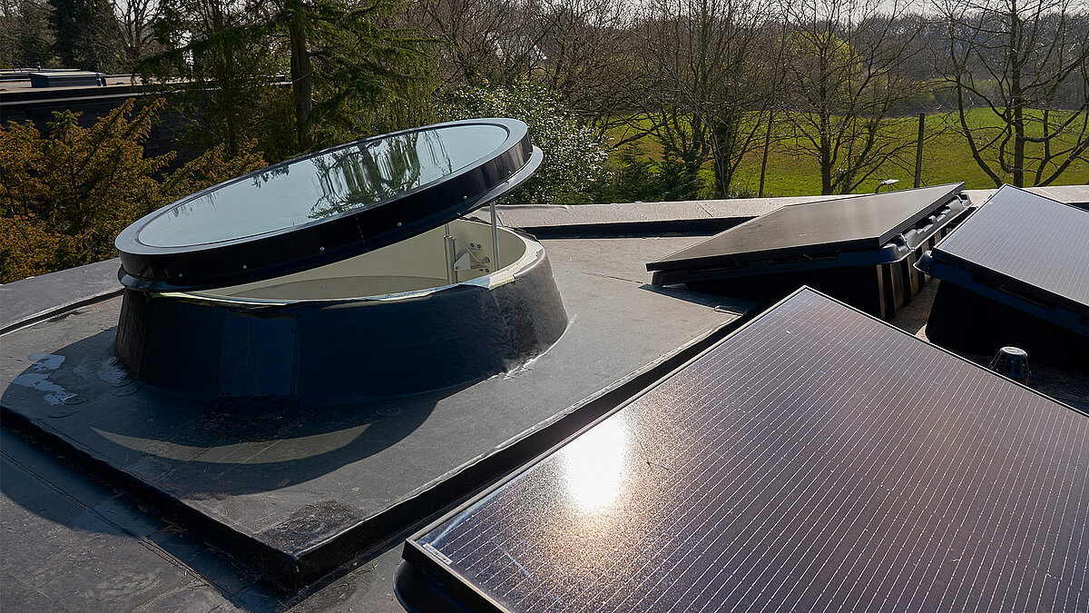 Open round LAMILUX rooflight on flat roof with solar modules