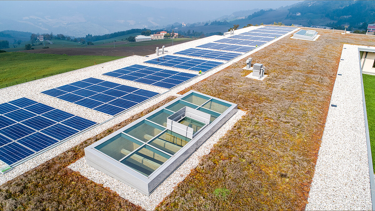 Blick von oben auf ein bepflanztes Dach mit Solarpanelen und zwei Glasdächern