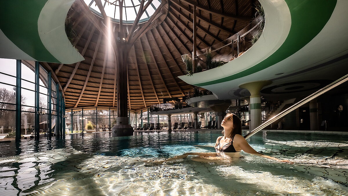 Interior of the Solemar thermal spa in Bad Dürrheim featuring a large glass dome and a woman relaxing in the water.