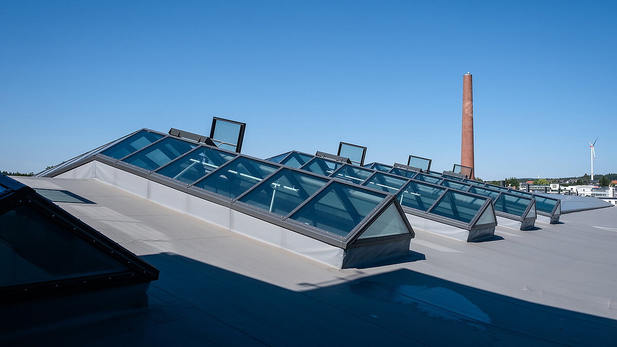 PR60 glass roof of Outlet Center Selb with open window elements and a chimney in the background.