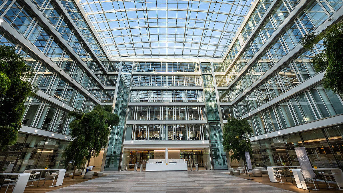 Interior view of the Newton office building of the TÜV Süd Group with a modern glass roof, large windows, and a green atrium.